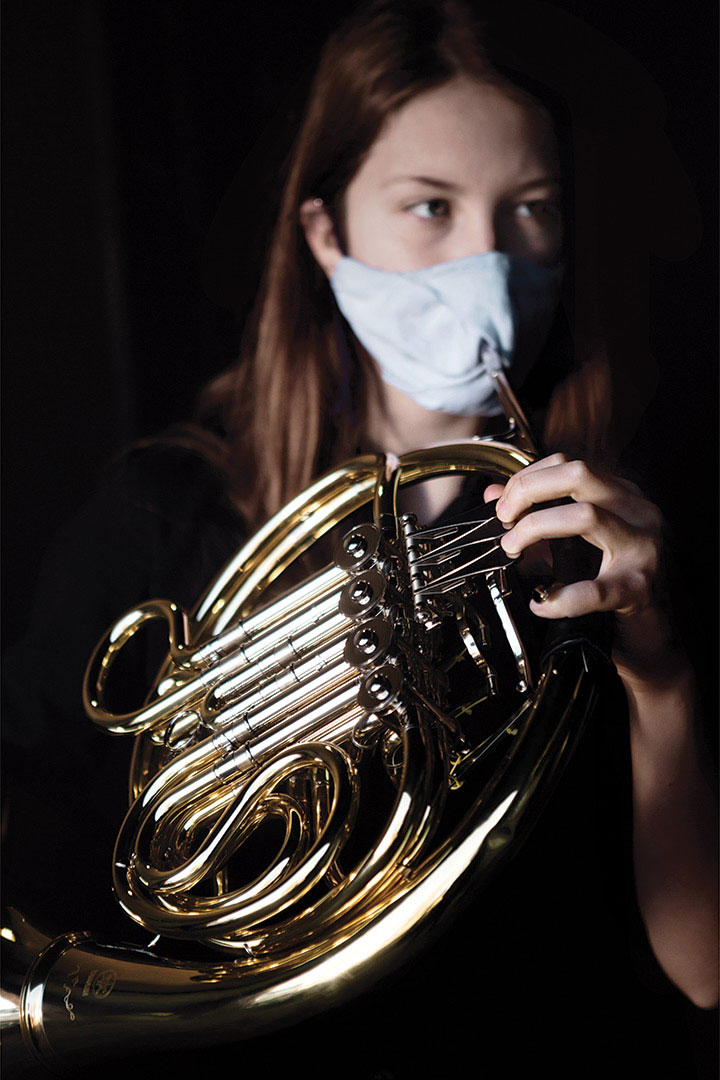 Masked student holds French horn with bell cover