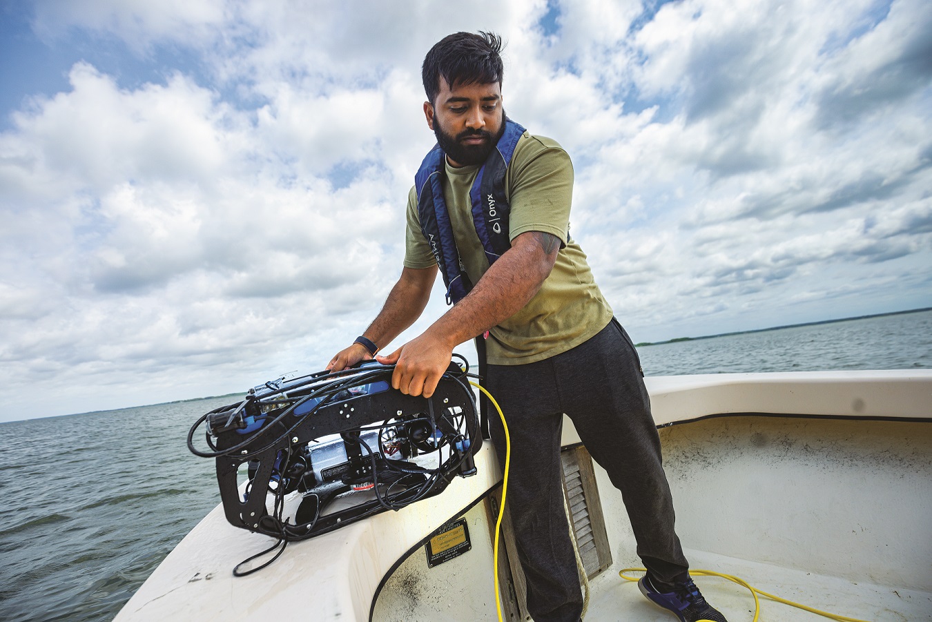 A researcher standing on a boat deck and holding a drone to put it into the water