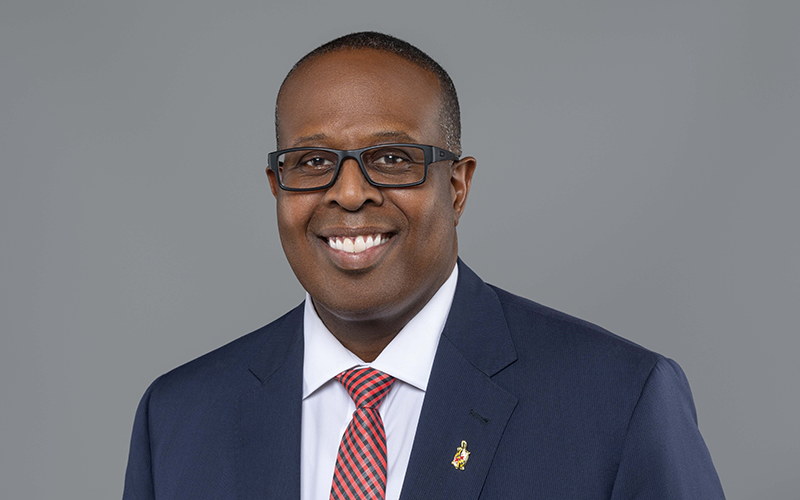 Dean Graham smiles while wearing a blue suit and red tie for his headshot