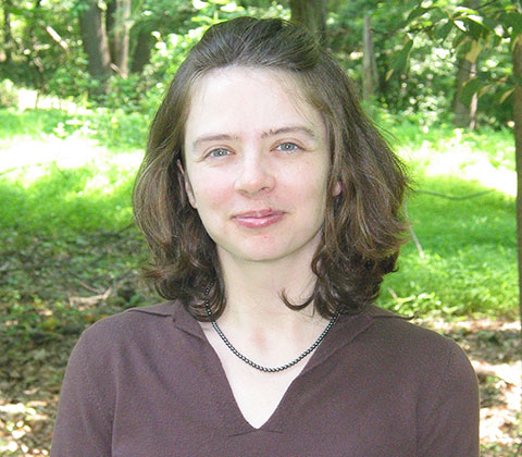 headshot of Pamela Abshire wearing a brown v-neck shirt and standing in front of green foliage