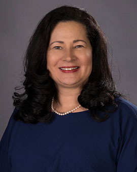 headshot of Sheila Cummings wearig a dark long-sleeved shirt with a pearl necklace