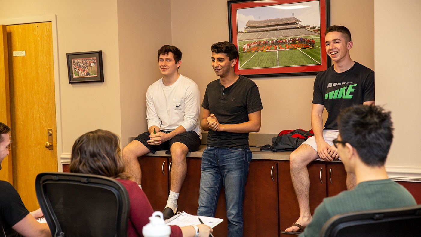 three students at the front of a room talking to other students