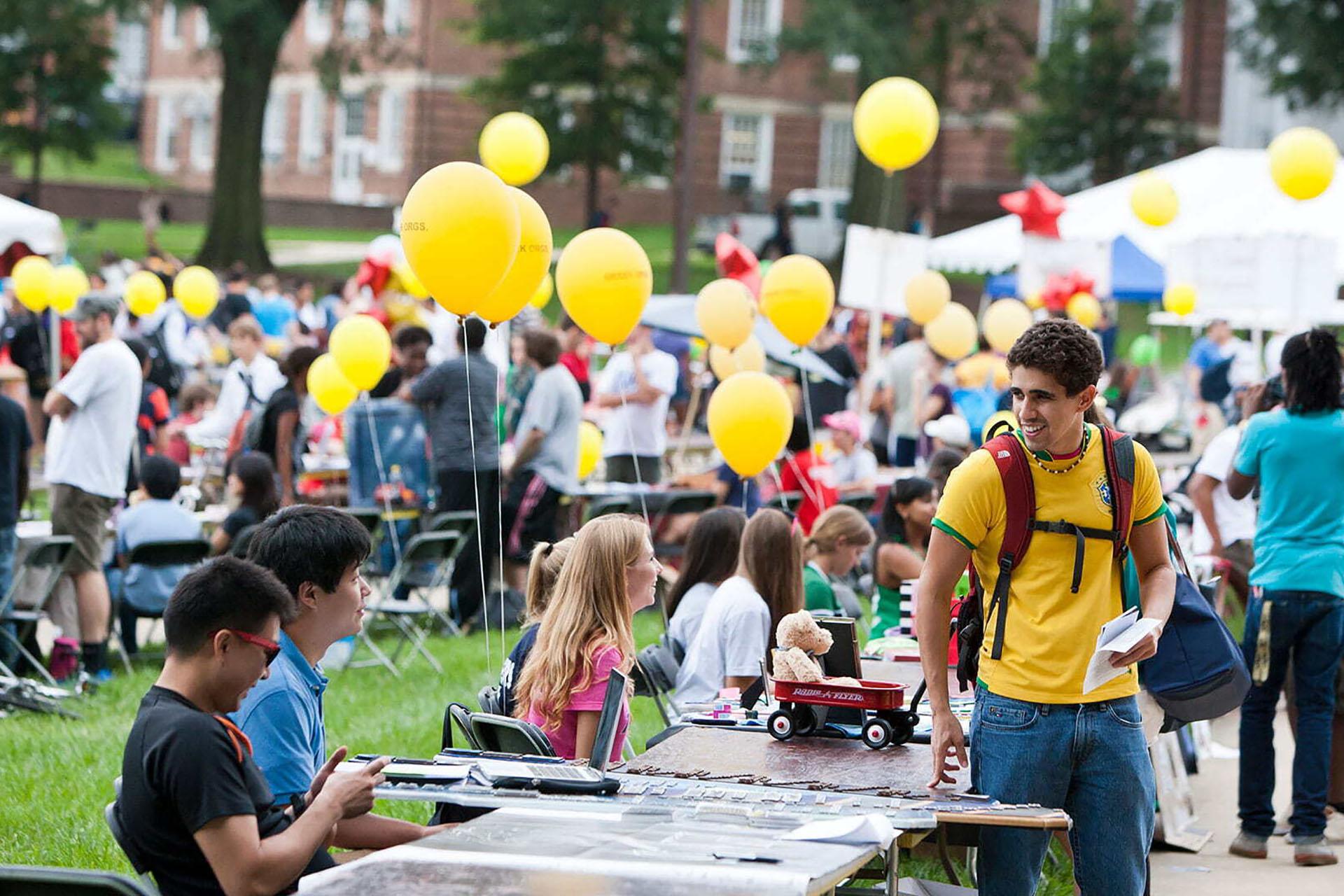 student wearing Brazil national soccer jersey checking out a booth during the first look fair, balloons and tents blurred in the background